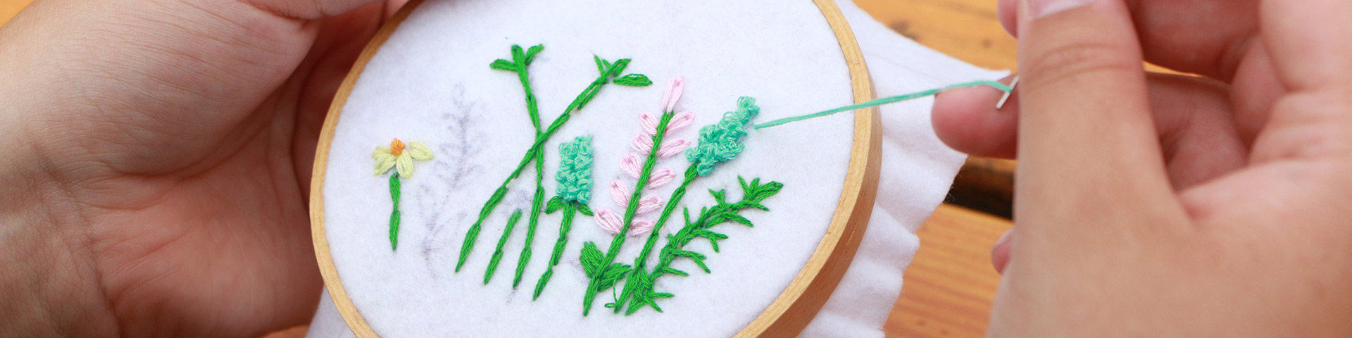 Close-up image of hands with needle and thread working on a floral embroidery design.