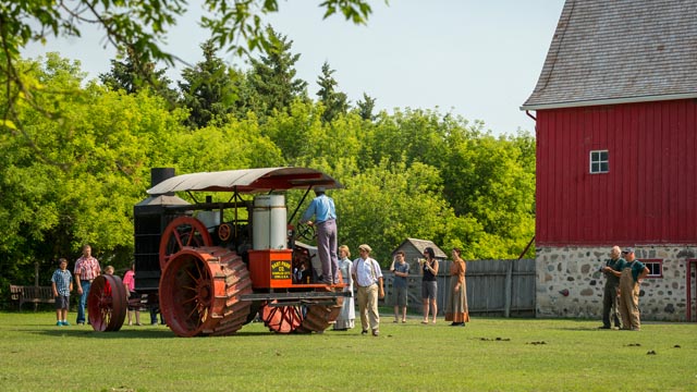 	Vue de loin d'un groupe de personnes s'approchant du tracteur Hart-Parr dans l'enclos près de la grange du lieu historique national du Homestead-Motherwell