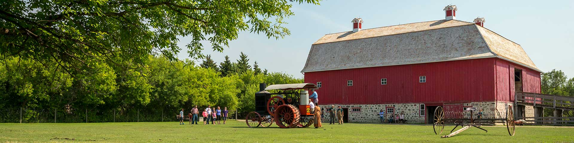 A distance view of a group of people in the barnyard learning about the Hart Parr tractor at Motherwell Homestead National Historic Site.