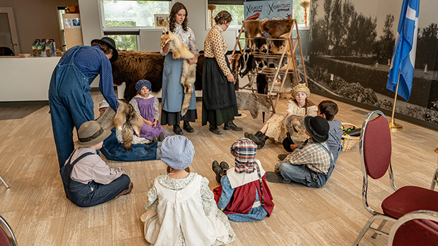Des campeurs de jour sont assis en cercle sur le sol et écoutent un interprète de Parcs Canada leur montrer différentes fourrures d’animaux.