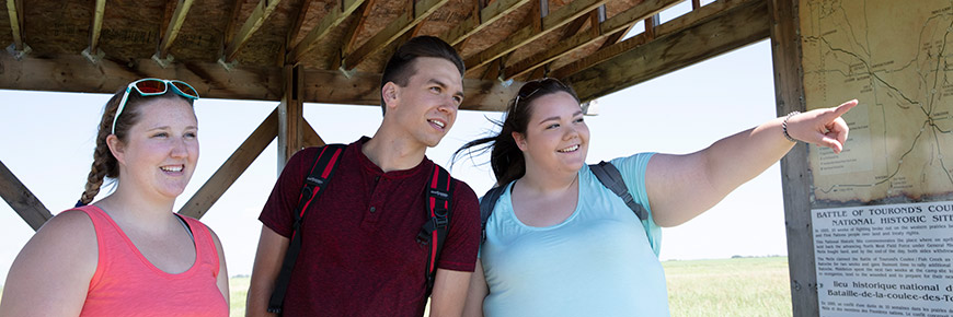 Three young people are looking over the historic site and related interpretive displays.