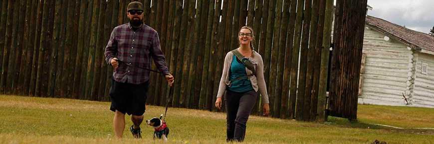 A man and woman walking a dog near a fort.