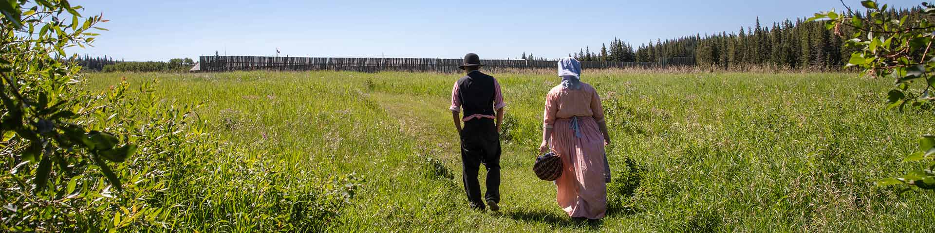 Deux interprètes costumés marchent le long d’un sentier fauché en direction du lieu historique national de Fort-Walsh.