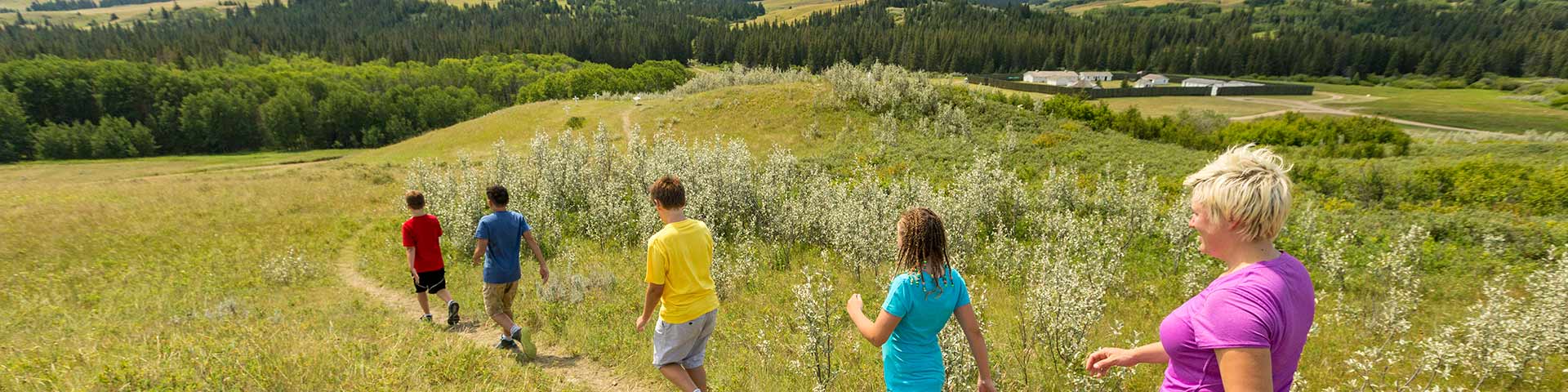 A family walking along a path with a view of Fort Walsh National Historic Site in the Cypress Hills in the background