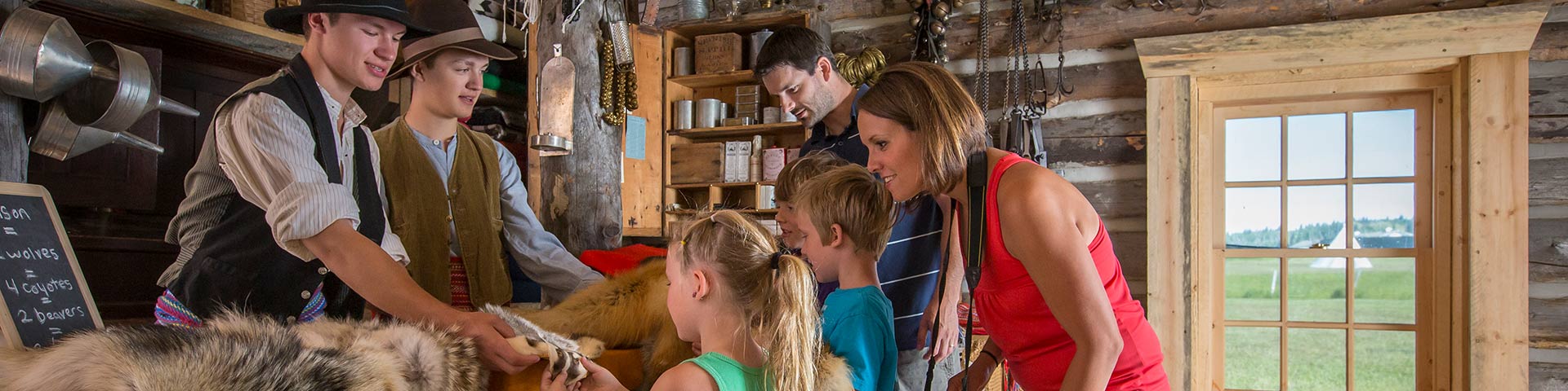 Famille regardant la marchandise offerte dans une cabane de traite métisse, avec l'aide de deux interprètes costumés, au lieu historique national du Fort-Walsh