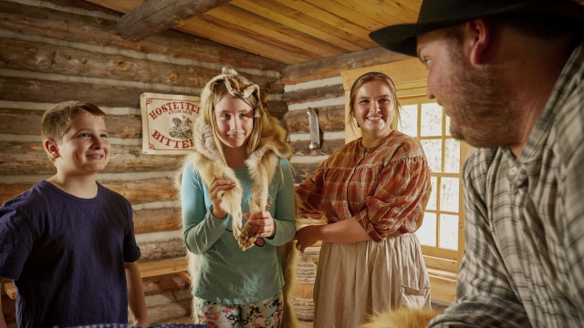 A family checking out the wares in the Métis trading cabin with the help of a couple of costumed interpreters at Fort Walsh National Historic Site.