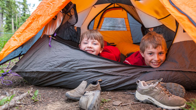 Two children smiling from the door of a tent
