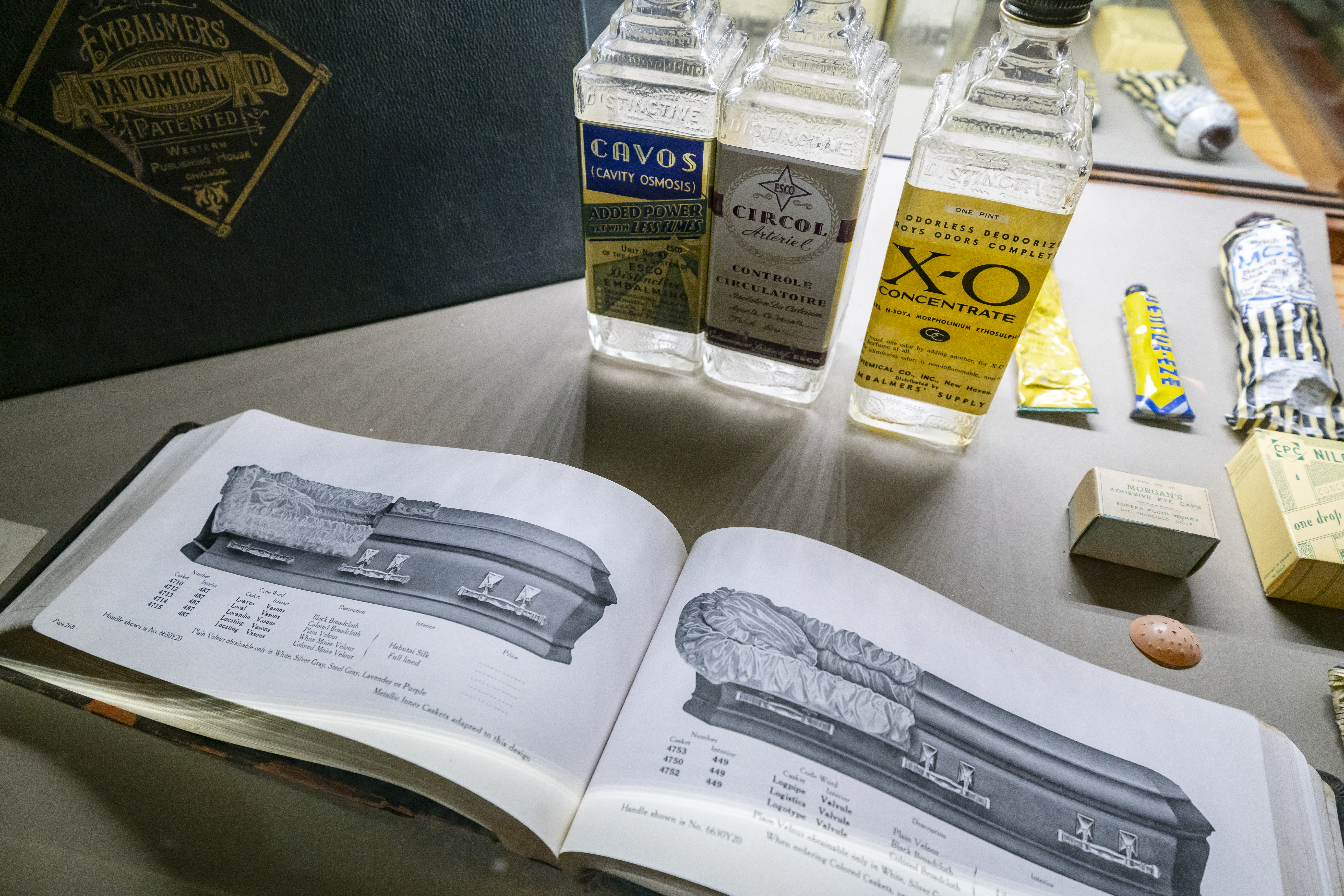livre ouvert affichant des cercueils sur une table avec des bouteilles de produits chimiques antiques