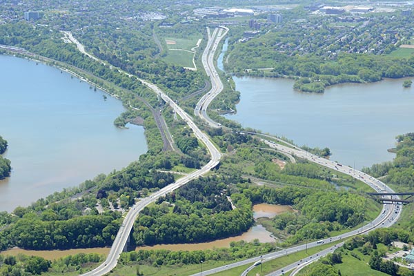 Aerial view of a narrow strip of wooded land bordered by water and crossed by roads and highways connecting urbanized areas