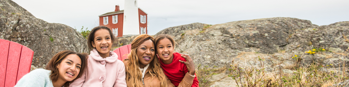 A family enjoying time together at the Red Chairs, with Fisgard Lighthouse behind. Fisgard Lighthouse National Historic Site.