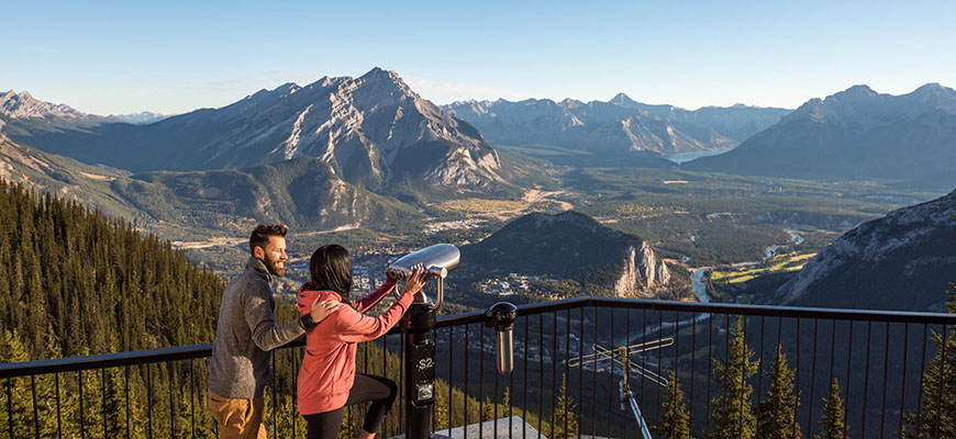 A couple takes in the view of the town of Banff and Cascade Mountain during sunrise on the Sulphur Mountain boardwalk. Banff National Park.
