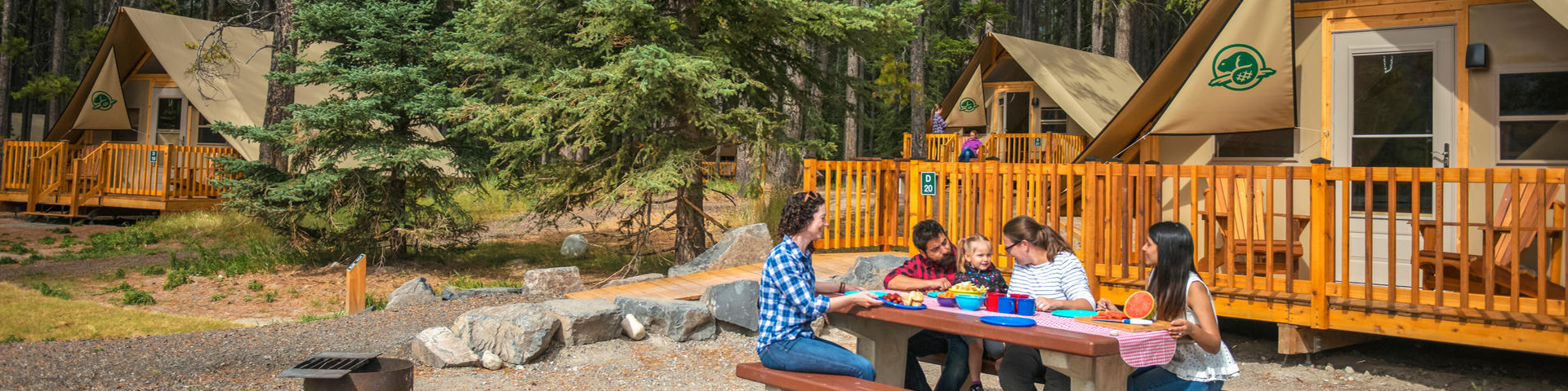 family sitting at picnic table in front of otentik campsite