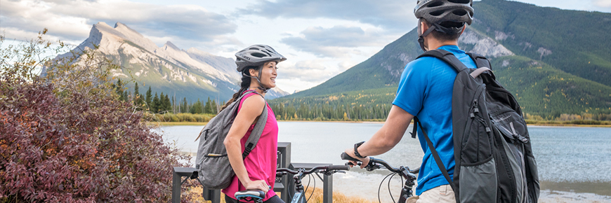 couple looks over Vermilion Lakes in Banff National park, wearing helmets. Top of bikes can be seen at the bottom of the image. 