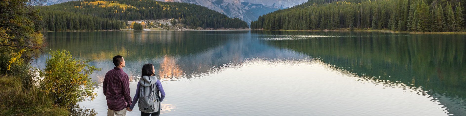 A couple enjoys the scenic view of Two Jack Lake from Two Jack Lakeside Campground during sunrise on a fall morning. Banff National Park.