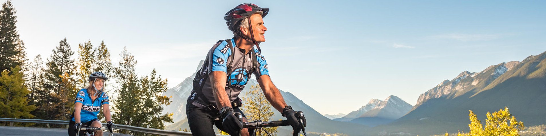 Two road cyclists ride down the Norquay road on a fall morning with Mount Rundle in the background. Banff National Park.