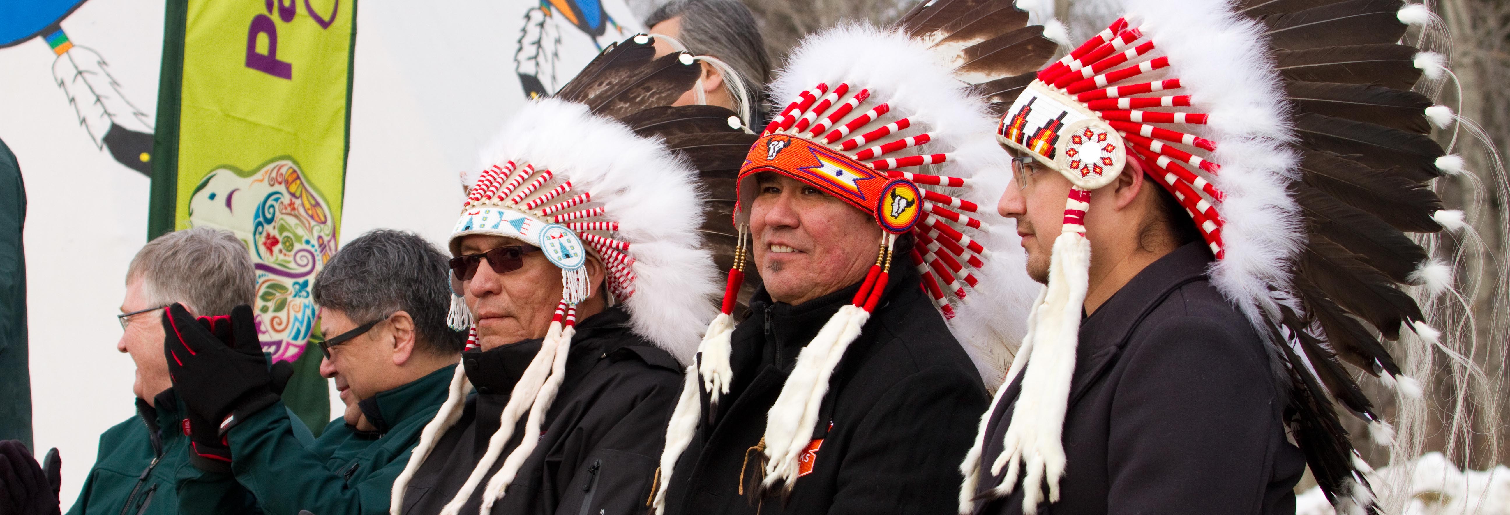 Aboriginal elders sit in a row wearing headdresses during a First Nation Ceremony. 