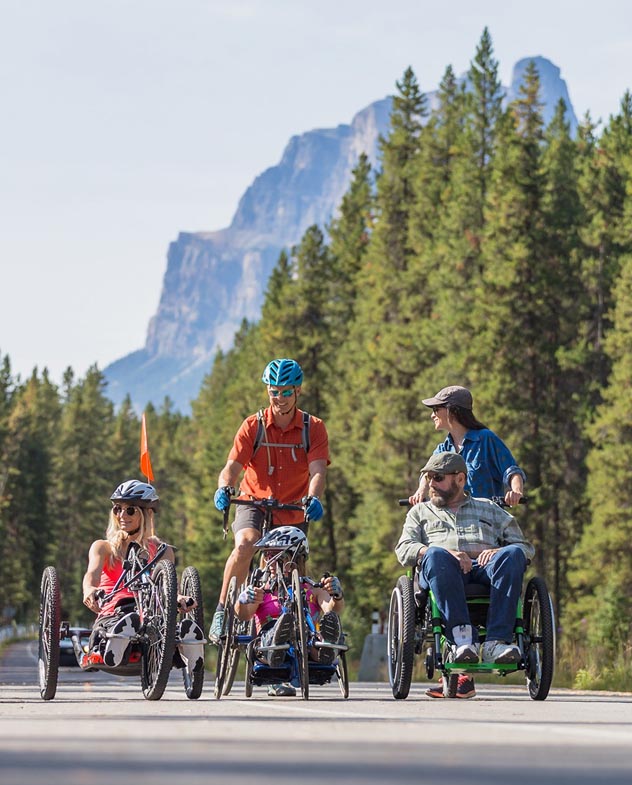 Cyclists using adaptive bicycles on a paved mountain path