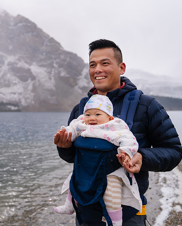 Homme avec un bébé sur sa poitrine debout à côté d'un lac