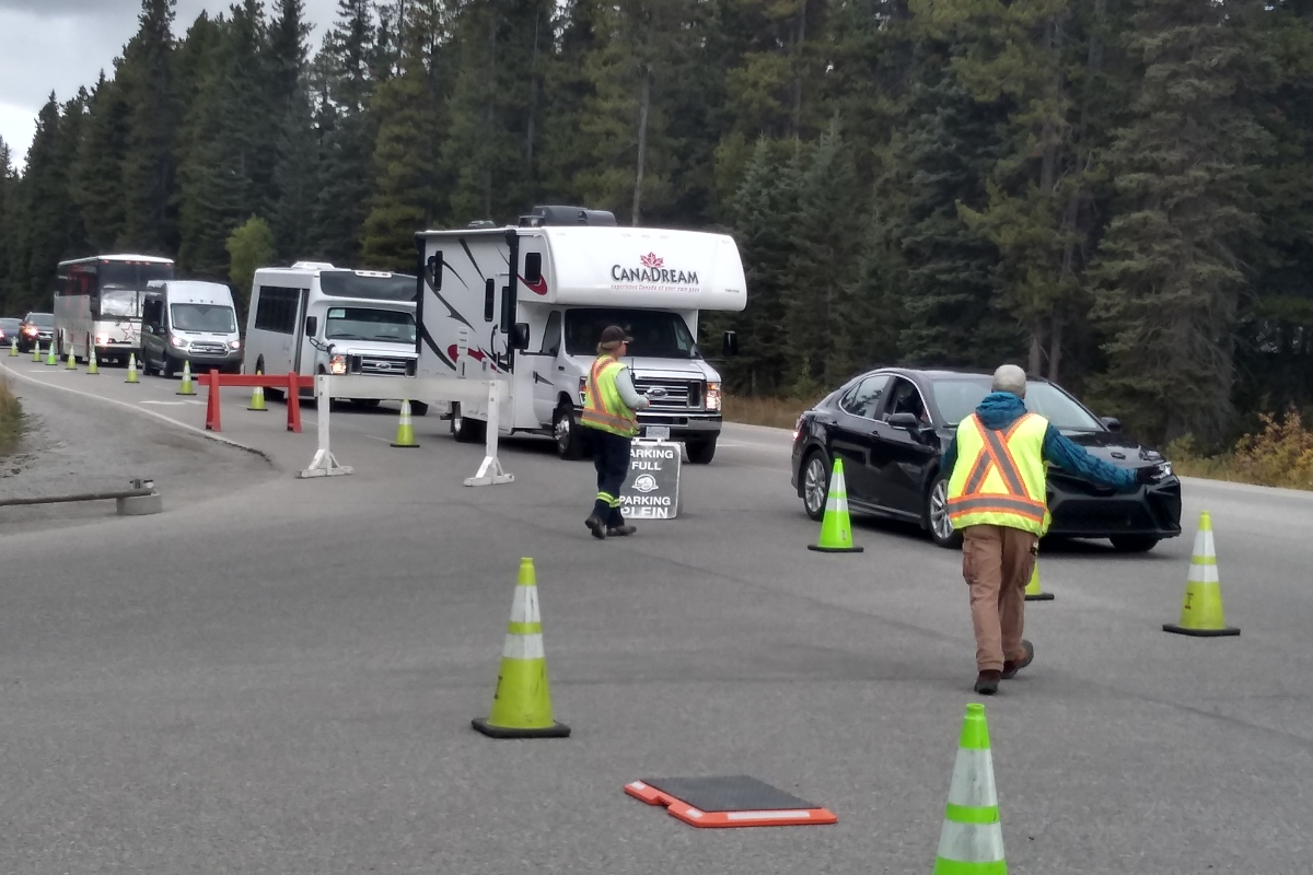 Deux signaleurs redirigent une file de véhicules à l’aide de leurs mains, de cônes et de panneaux de signalisation.  