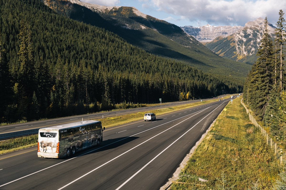 A bus and van travel along a highway through the mountains.