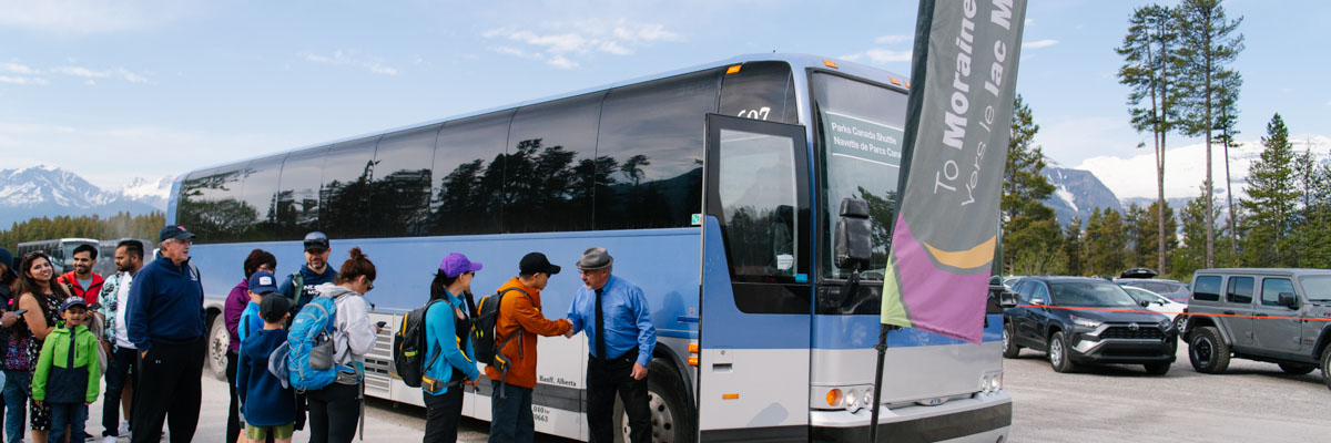 A group of visitors are greeted by a bus driver as they board a Parks Canada shuttle