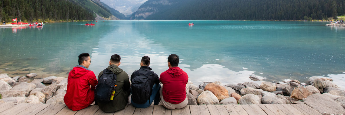 Four visitors face away from the camera looking at canoes on Lake Louise