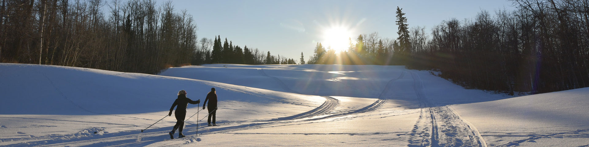 Un skieur de fond se déplace en descente sur une piste damée alors que le soleil commence à se coucher à la fin d’un jour d'hiver.