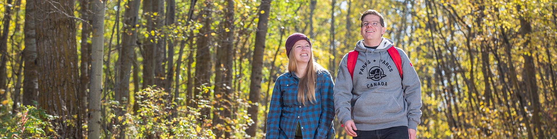 A young adulte couple walk down a leaf covered trail during the fall at Astotin Lake Recreation Area in Elk Island National Park.