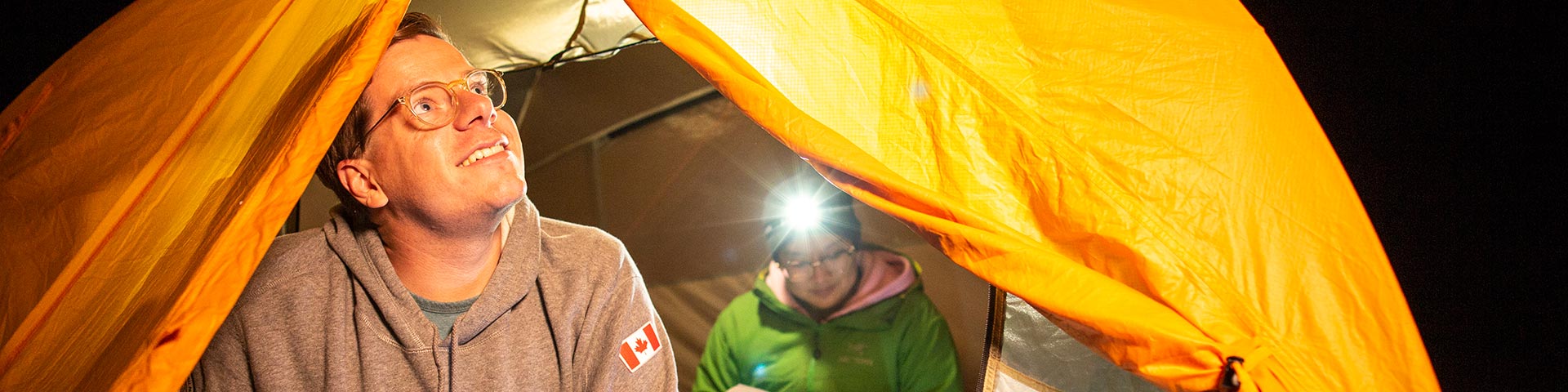 A young man looks out of his tent while a women reads a book at Oster Lake Backcountry Campground in Elk Island National Park.