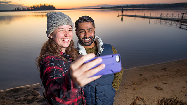 	Un jeune couple prend un égoportrait sur la plage pendant le coucher du soleil au lac Astotin, dans le parc national Elk Island