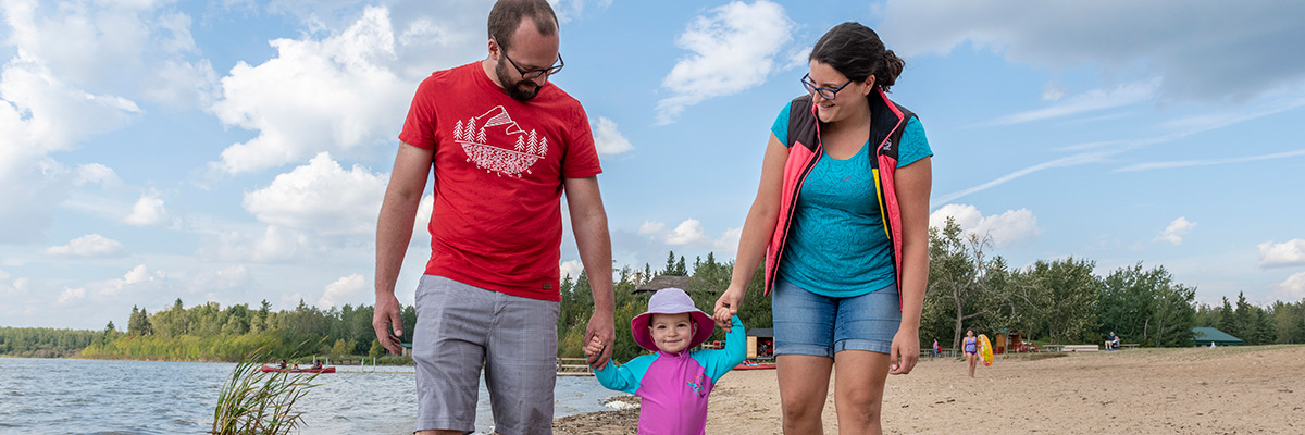 A young family walk in the sand on the shore of Astotin Lake... Elk Island National Park