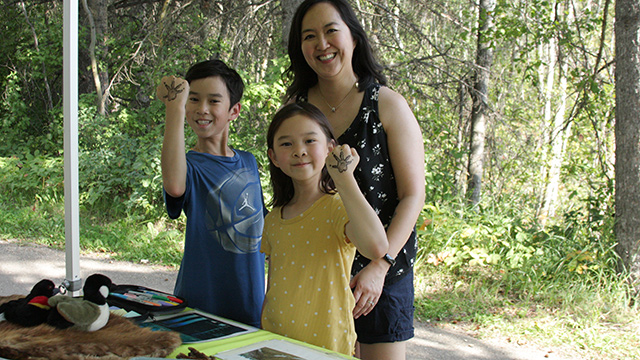 A family is gathered smiling. Two children hold up their hands to show beaver footprint stamps.