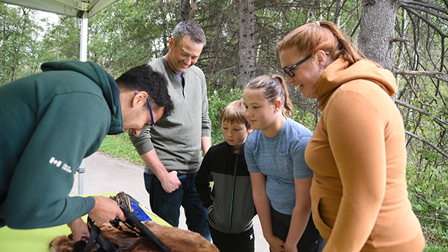 A family gathers around an interpreter to watch a video of a beaver on an iPad.