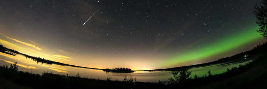 A shooting star falls across a starry sky and the northern lights. 