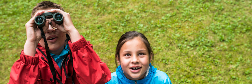 Two children look up in awe through binoculars. 