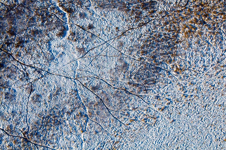 Photo aérienne d’un paysage enneigé gravé de sillons formés par des sentiers, rappelant des réseaux de cours d’eau ou des vaisseaux sanguins.