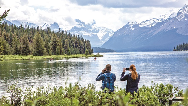 Two adults taking phone photos of a picturesque landscape.