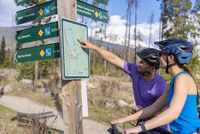 Two bikers look at a trail sign.