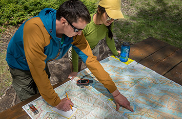 Deux adultes près d’une table de pique-nique regardent une carte, l'un d'eux pointe quelque chose du doigt.