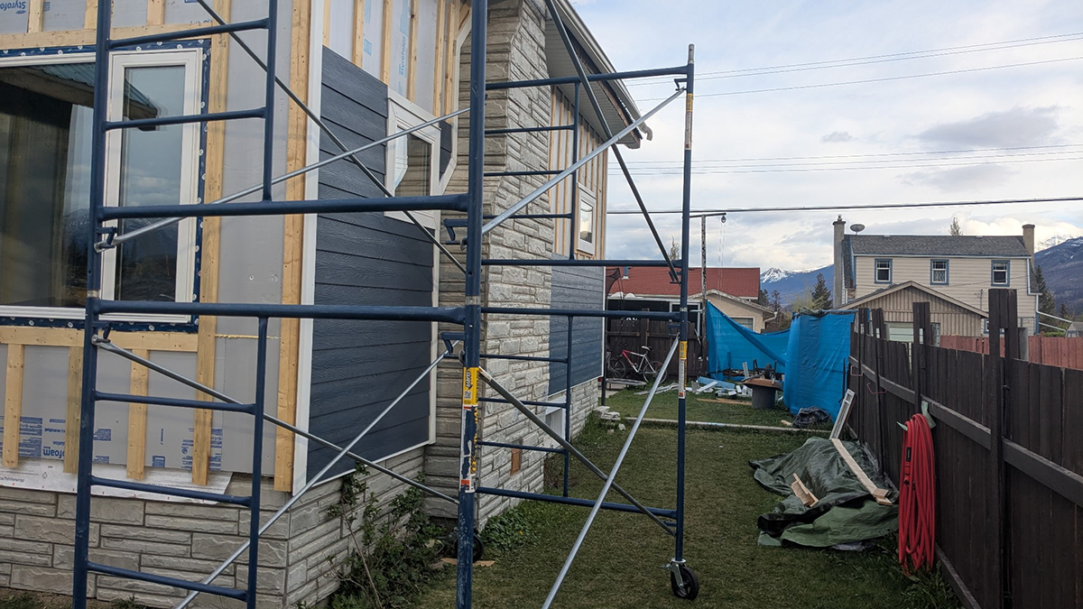 A house with non-combustible cladding installed following damage to the Jasper Wildfire. The yard contains construction equipment and other houses are visible in the background.