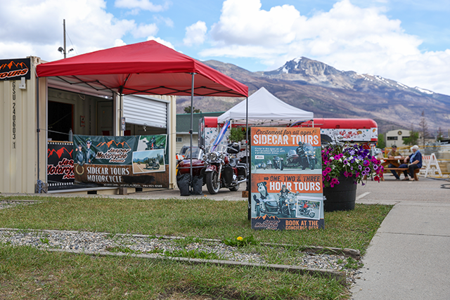 Pop-up business village with a red tent and a white tent behind it, featuring posters promoting sidecar tours.