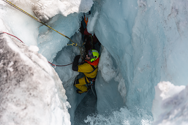 A Parks Canada visitor safety staff member descending into a very narrow crevasse, equipped with ropes, gloves, and a helmet.