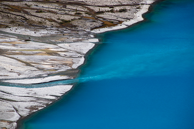 A close-up view of Peyto Glacier's vibrant blue waters on the left side, with rugged bedrock formations visible on the right side.