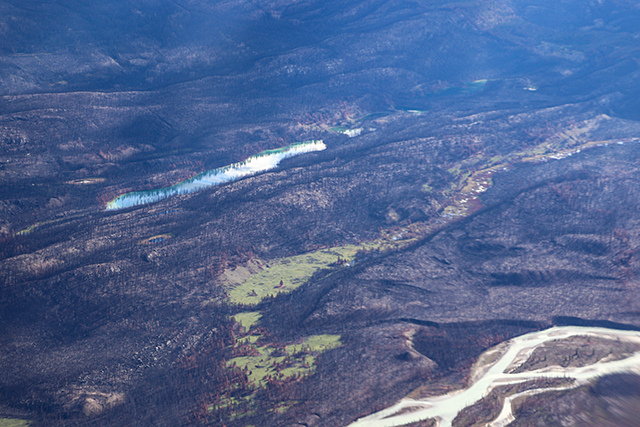 A bird's-eye view of the terrain, featuring a long and narrow, finger-shaped lake surrounded by meadows.