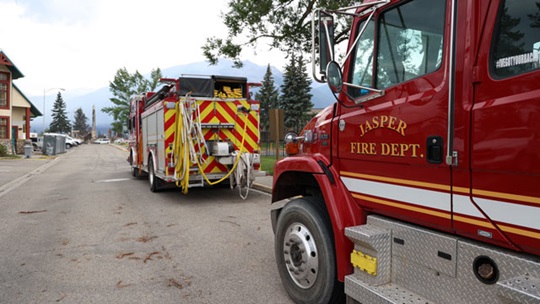 Deux camions du service incendie de Jasper s’éloignent sur une route en ville.