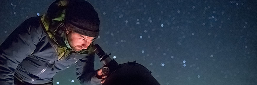 A person looks into a telescope under the back drop of a star filled night