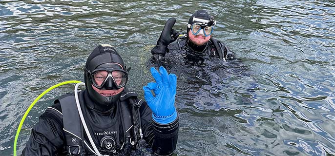 Une personne portant des lunettes de soleil au bord de l’eau fait le signe de la paix avec sa main.