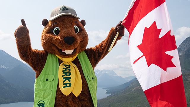 Parka, la mascotte de Parcs Canada, tient un drapeau canadien