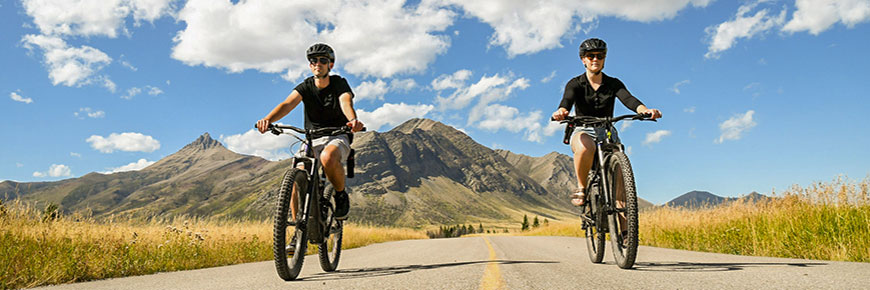 Deux personnes à vélo de montagne descendent un sentier avec une montagne en arrière-plan.