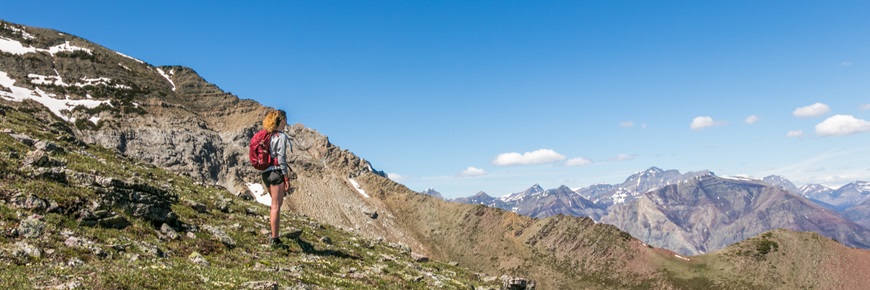 A hiker on a mountain side looks of into a valley of mountains.